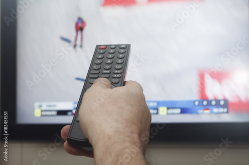 мужская рука с пультом управления на фоне  телевизора со спортивной передачей