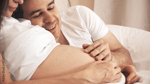 Man stroking pregnant wife's belly in bed at home