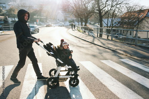 Father and child boy in stroller cross a road. photo