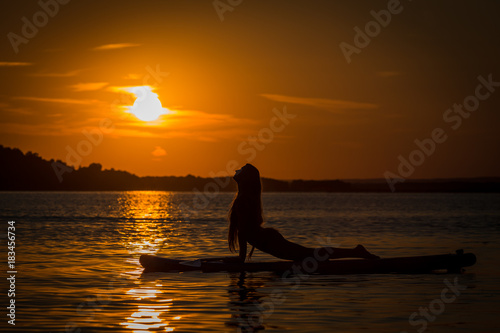 Silhouette of beautiful young girl exercising yoga on SUP in the scenic yellow sunset on lake Velke Darko, Zdar nad Sazovou, Czech republic photo