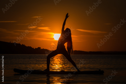 Silhouette of beautiful young girl exercising yoga on SUP in the scenic yellow sunset on lake Velke Darko, Zdar nad Sazovou, Czech republic