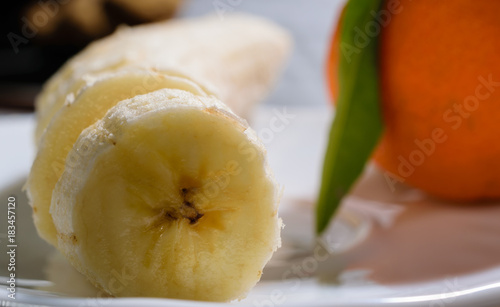Sliced banana on a white plate with mandarin orange in the background