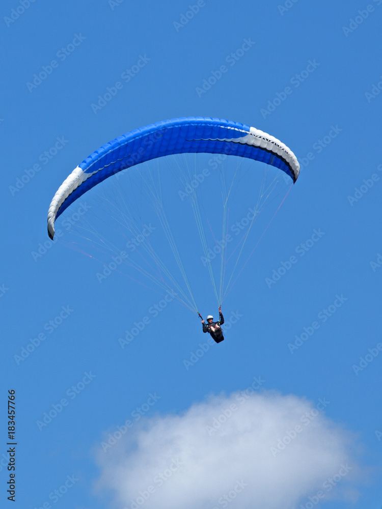 Vol en parapente avec aile bleue sur fond de ciel bleu d'été au-dessus des nuages.