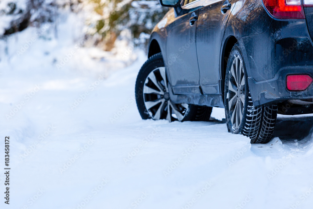 Naklejka premium Winter tires. Black SUV car rear view on snowy forest road. Winter conditions.