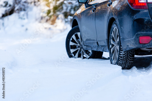 Winter tires. Black SUV car rear view on snowy forest road. Winter conditions.