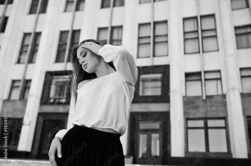 Portrait of a fabulous young successful woman in white blouse and broad black pants posing on the stairs with a huge white building on the background. Black and white photo. Portrait of a fabulous young successful woman in white blouse and broad black pants posing on the stairs with a huge white building on the background. Black and white photo.