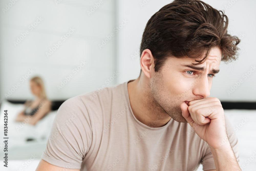 Fototapeta premium Portrait of sad brunette man sitting in bed at home