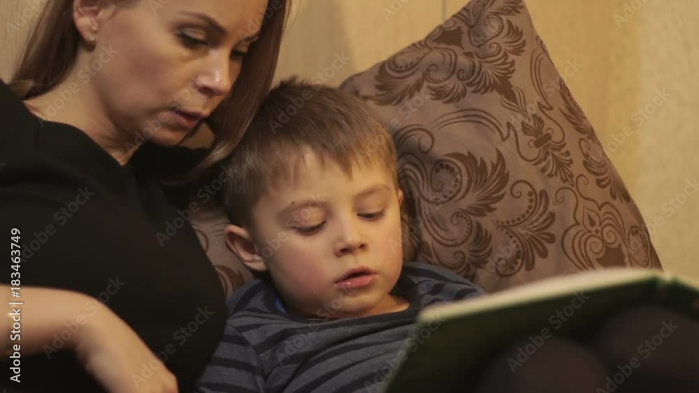 Young mother together little son reading a book lying on bed in cozy bedroom Young mother together little son reading a book lying on bed in cozy bedroom