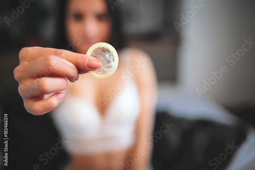 Woman showing a condom on bed, Focus on the condom in the foreground