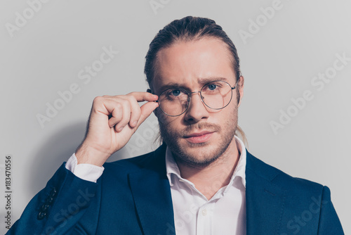 Close up portrait of attractive man holding with one hand glasses on face with serious expression, standing over grey background