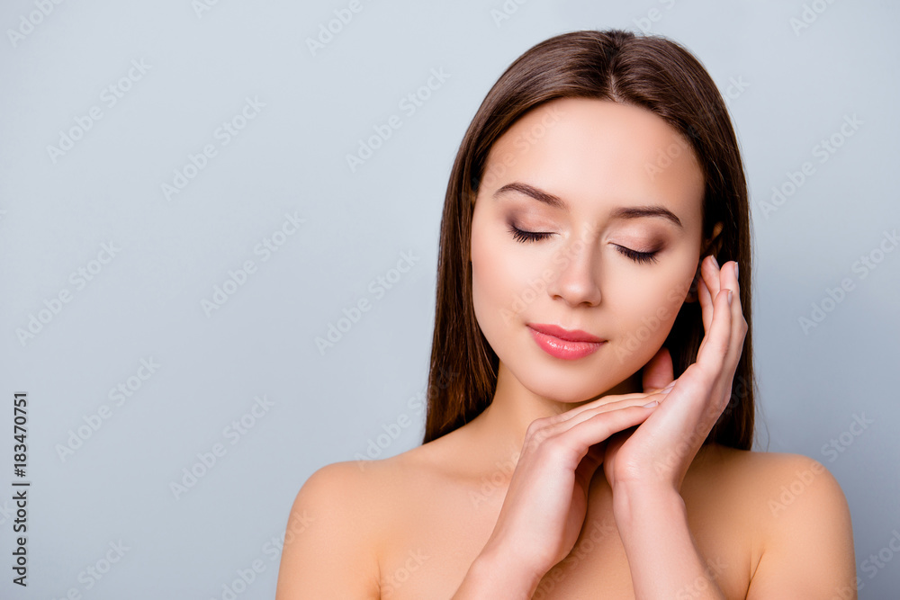 Close up photo of happy smiling beautiful girl with closed eyes touching her smooth skin after applying moisturizing lotion, isolated on grey background, copyspace Close up photo of happy smiling beautiful girl with closed eyes touching her smooth skin after applying moisturizing lotion, isolated on grey background, copyspace