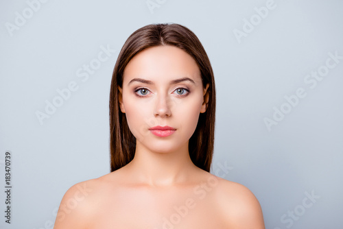 Close up portrait of confident young charming woman with dark hair, clean flawless skin, natural lips and naked shoulders, isolated on grey background