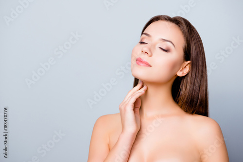 Concept of having perfect skin without wrinkles. Beautiful young woman is enjoying her smooth flawless skin, she is touching her neck, isolated on grey background, copy space