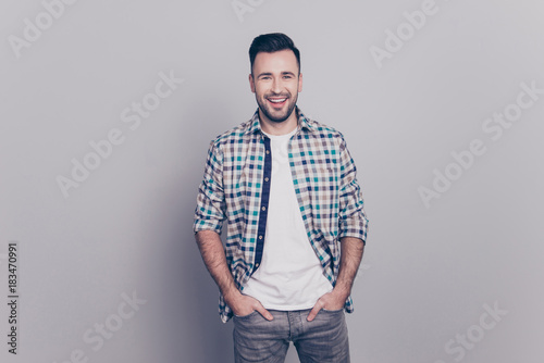 Portrait of cheerful, attractive, smiling man holding hands in pocket of jeans looking at camera standing over grey background