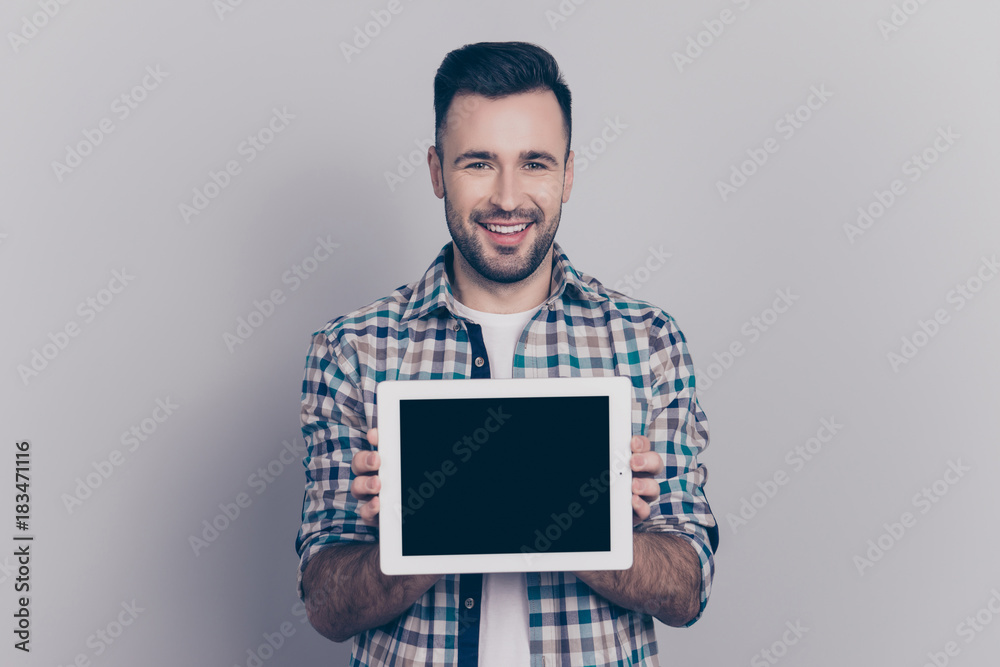 Portrait with copy space of young, smiling, cheerful man showing black tablet screen, presenting a gift, present, using, choosing modern electronic device, standing over grey background