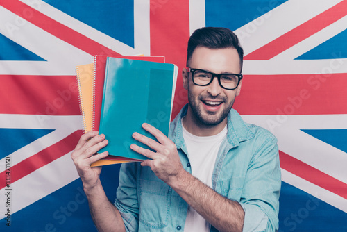 English language learning concept-portrait of cheerful attractive man with bristle showing colorful copy books standing over English flag background photo