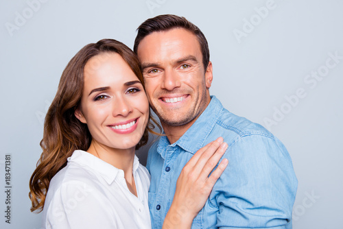 Close up portrait of mature, adult, attractive, cute, lovely couple with beaming smiles, check to check face, looking at camera, over grey background
