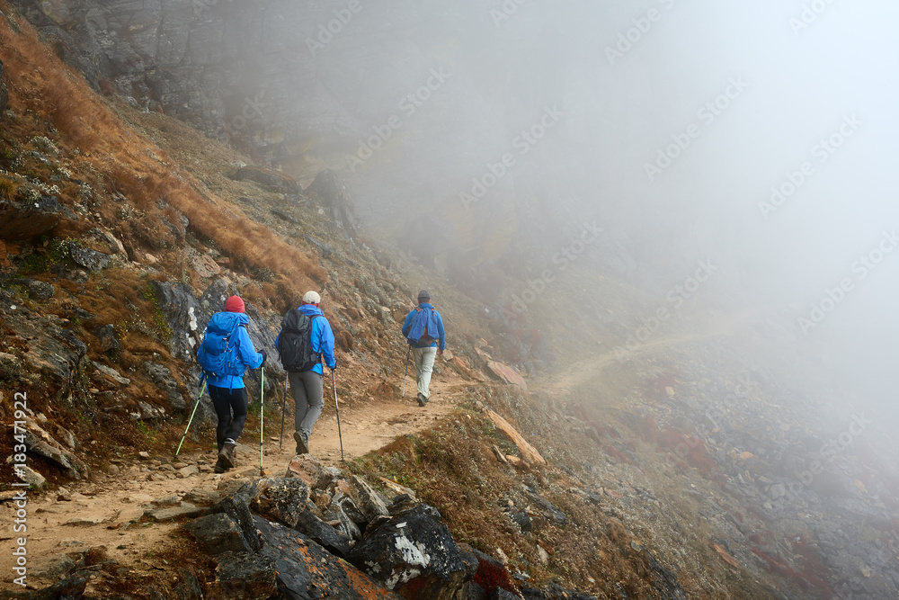 Group Hikers with Backpacks walking down on Mountain Trail in foggy mountains. Group Hikers with Backpacks walking down on Mountain Trail in foggy mountains.