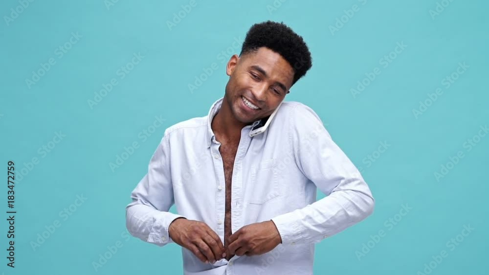 Smiling african man talking by smartphone while puts on a shirt over blue background Smiling african man talking by smartphone while puts on a shirt over blue background