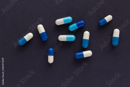 Heap of pills spreaded over color table. Group of assorted white and blue tablets. Black background.