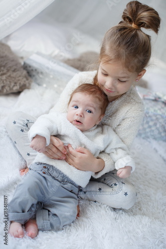 Little girl embracing a newborn baby brother.Little girl and baby boy,brother and sister playing in parents bed.Cute girl and a newborn boy resting together in a white bedroom.
