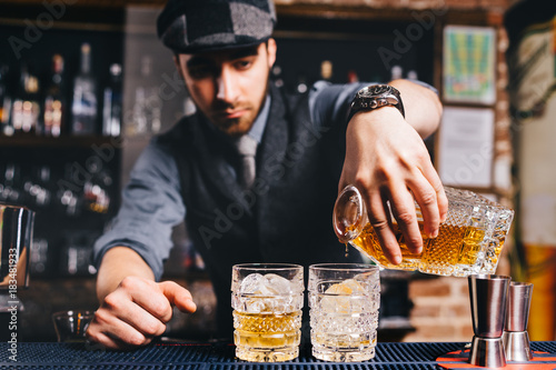 Obraz na plátně Barman pouring whiskey cocktail in crystal glasses