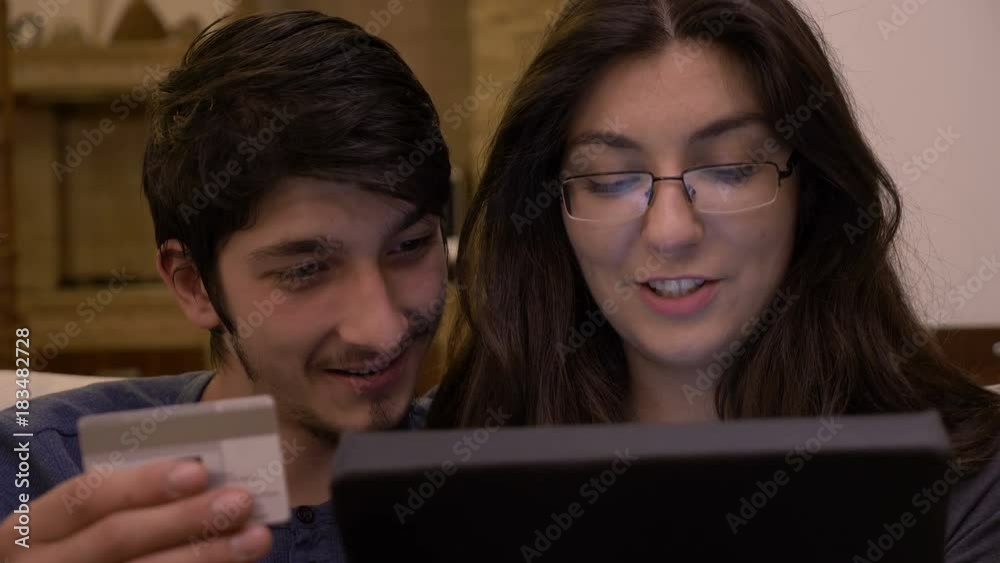 Affectionate kissing young couple at home using tablet pc introducing credit card information to shop online Affectionate kissing young couple at home using tablet pc introducing credit card information to shop online