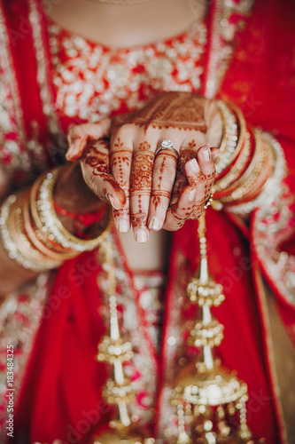Tender hands of an Indian bride covered with henna tattoo while she dressed in red lehenga with golden embroidery