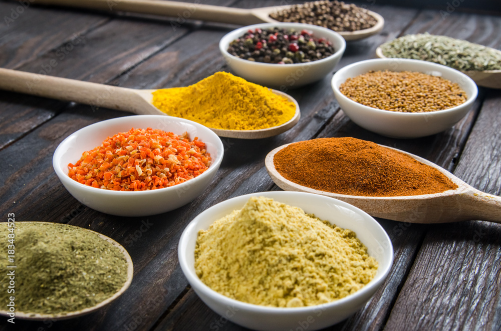 different spices in wooden spoons on a black wooden background