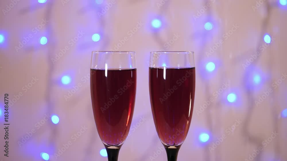 New year and christmas celebration with red wine. Holiday decorations with flute glass, and blinking garland. Close-up. Abstract blurred christmas lights bokeh background.