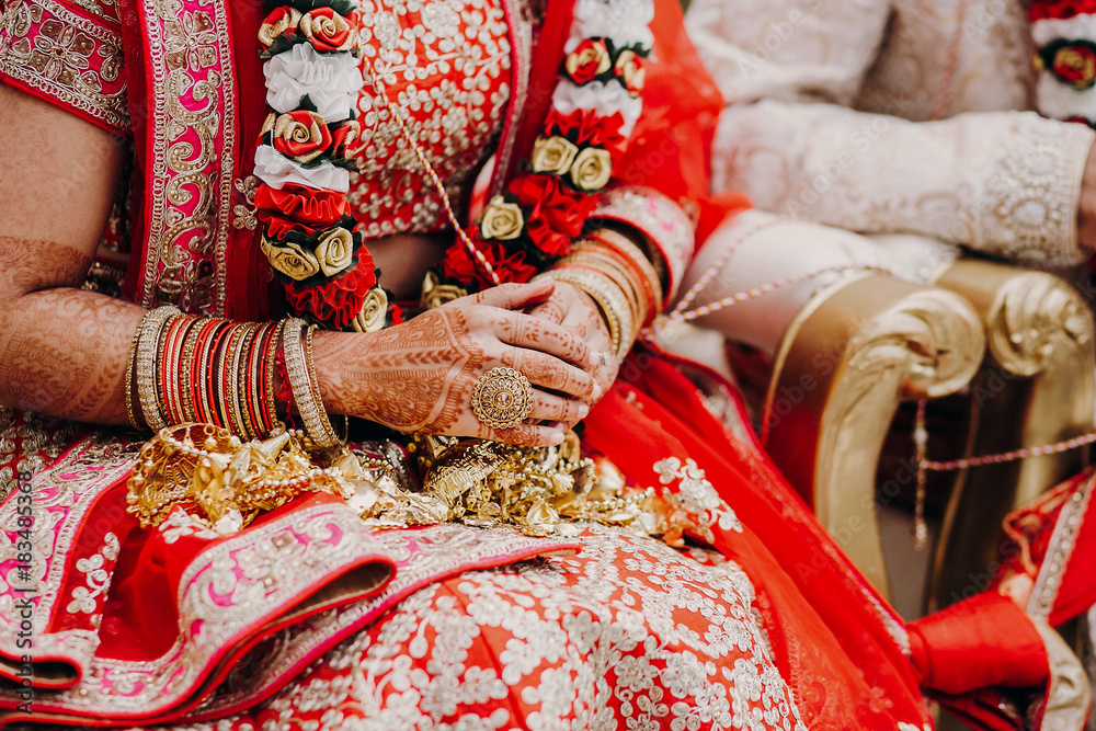 Stunning Indian bride dressed in Hindu traditional wedding clothes lehenga embroidered with gold and a veil during Saptapadi ceremony holds golden accessories on her knees