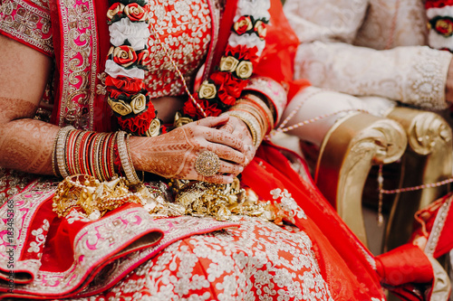 Stunning Indian bride dressed in Hindu traditional wedding clothes lehenga embroidered with gold and a veil during Saptapadi ceremony holds golden accessories on her knees