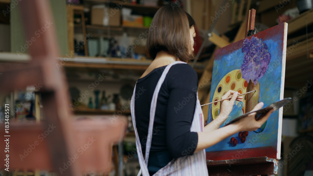 Talented young woman artist painting picture on canvas in art-class