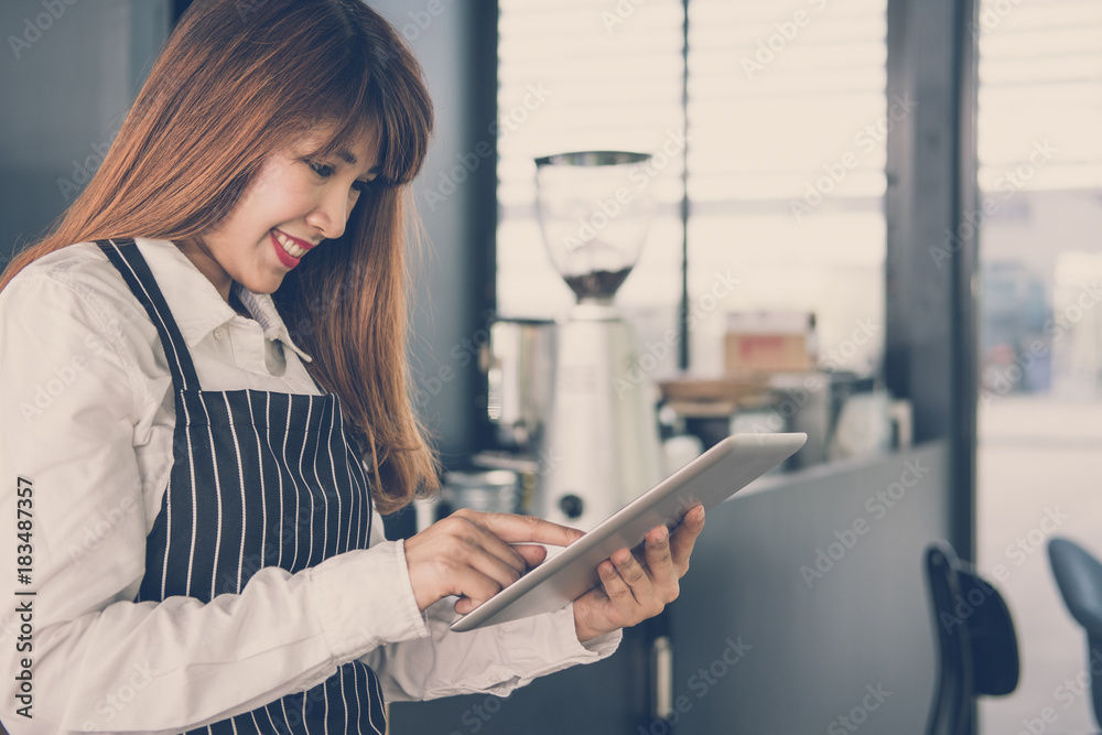 small business owner holding tablet at counter in coffee shop. female barista wearing apron using touchpad at bar in cafe. food service, restaurant concept. small business owner holding tablet at counter in coffee shop. female barista wearing apron using touchpad at bar in cafe. food service, restaurant concept.