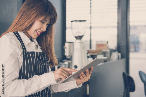 small business owner holding tablet at counter in coffee shop. female barista wearing apron using touchpad at bar in cafe. food service, restaurant concept.