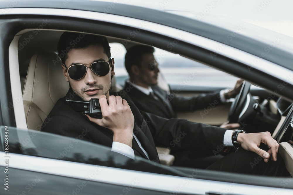 bodyguard in sunglasses talking by portable radio while sitting in car bodyguard in sunglasses talking by portable radio while sitting in car