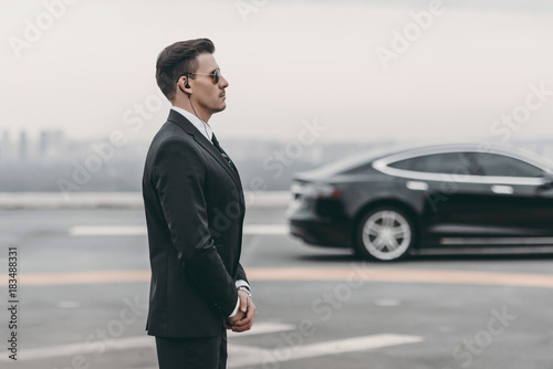 bodyguard in suit with security earpiece standing close to politician car photo