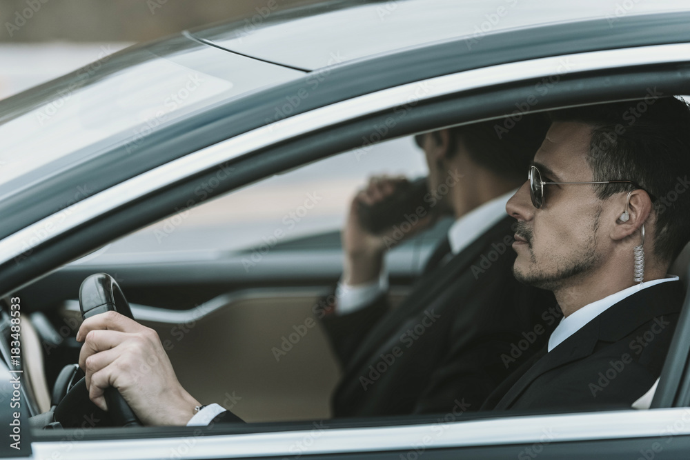 bodyguards with portable radio and security earpiece sitting in a car