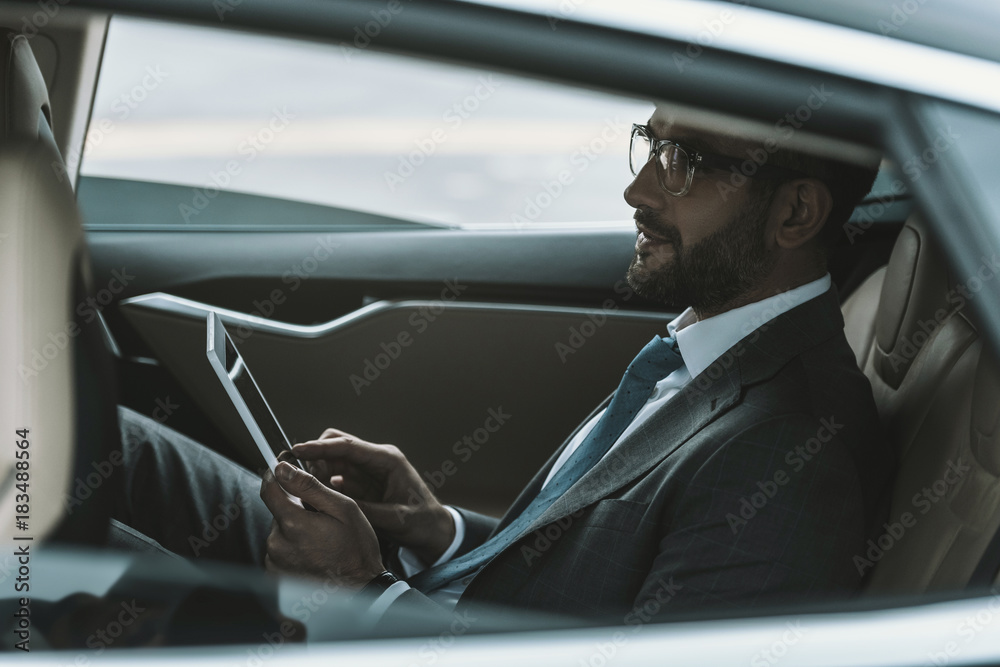 handsome businessman in glasses sitting in car and holding tablet in hands