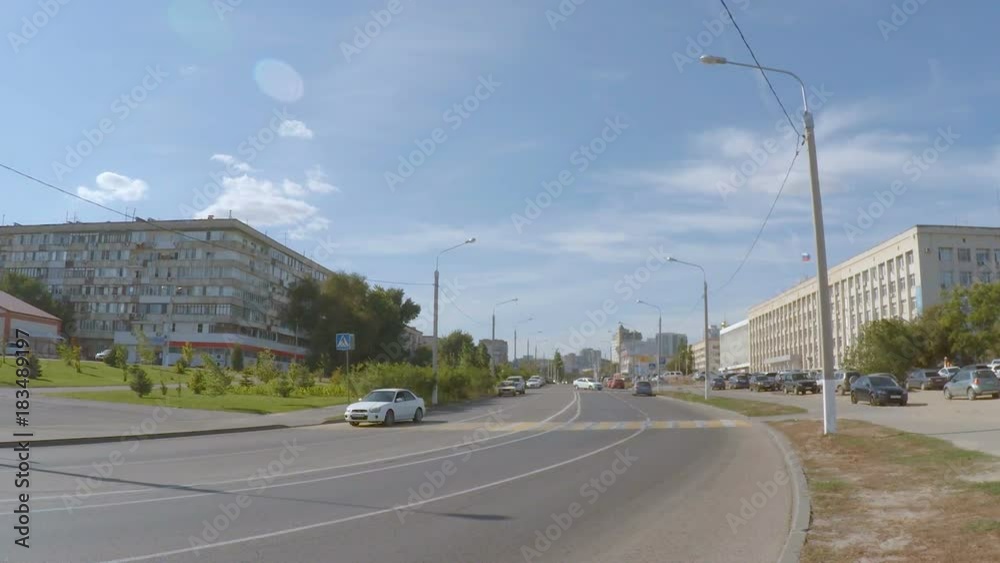 Cars are driving down the street of the city between the buildings. Blue sky with white clouds. Cars are driving down the street of the city between the buildings. Blue sky with white clouds.