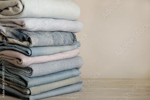 Pile of jeans and knitted clothes (sweaters, scarves, pullovers) blue, white and grey colors.