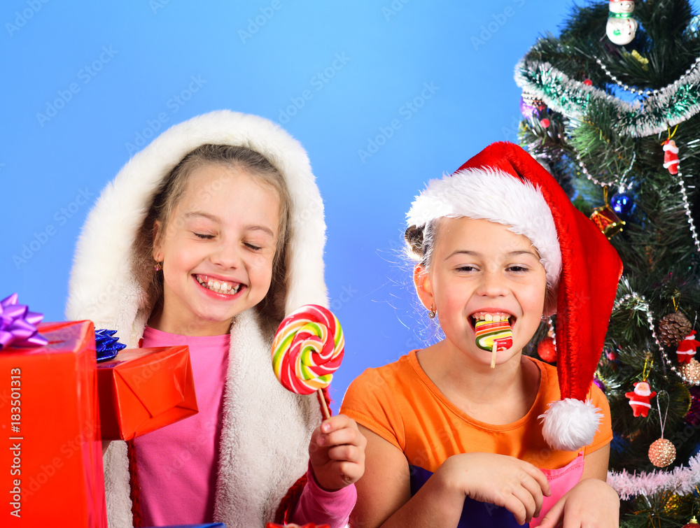 Kids in Santa Claus hats with gift boxes open presents.