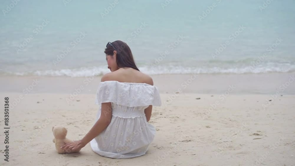 Asian single woman sitting with teddy bear at seaside beach friendship lonely everywhere on tropical sea and wearing white dress Asian single woman sitting with teddy bear at seaside beach friendship lonely everywhere on tropical sea and wearing white dress