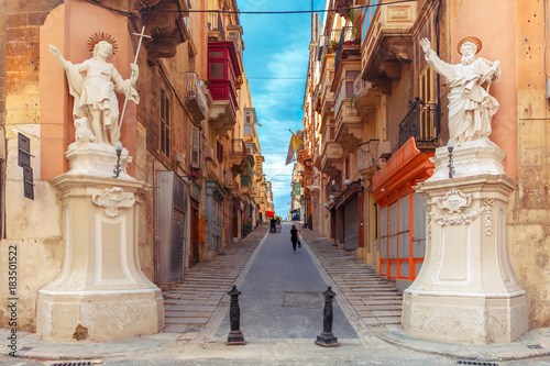 The traditional Maltese street stairs with corners of houses, decorated with statues of saints St. John and St. Paul and building with colorful balconies in Valletta, Capital city of Malta