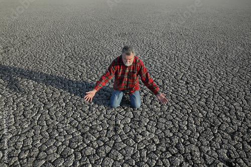 Desperate man kneeling at dry cracked land after drought, natural disaster