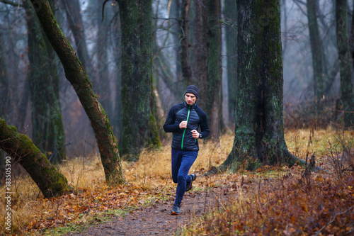 Young man jogging in fall park. Trail running in cold and misty weather © skumer