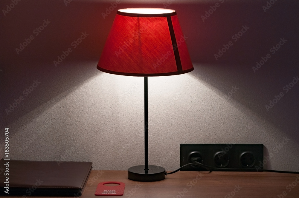 Intimate atmosphere in the hotel room. Bedside table on which lie the  leather folder of the menu, do not disturb the sign and the lamp with a  textile lampshade. Stock Photo