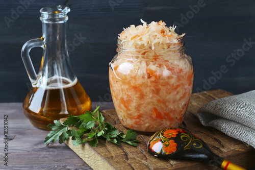 Jar of sauerkraut on wooden board and bottle of oil