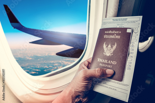 Business man holding passport and immigration form on seat next to windows on airplane vacation jorney. Hand holding passport with passport close up on plane windows background. photo