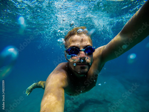 Underwater view of a young adventuristic attractive man swimming and enjoying at the sea for summer holidays while taking a selfie.